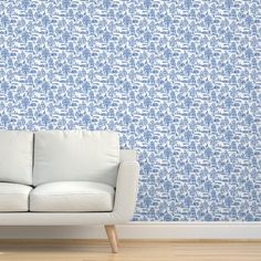 a white couch sitting in front of a blue flowered wallpaper on a wooden floor