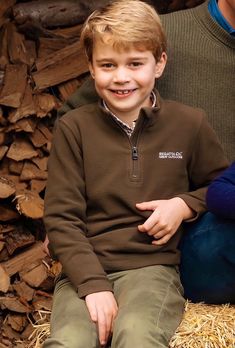 a young boy sitting on top of a pile of wood