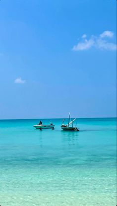 two boats floating on top of the ocean next to each other in clear blue water