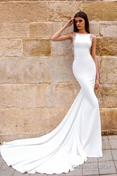 a woman in a white wedding dress leaning against a stone wall with her hand on her head