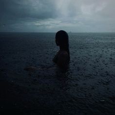 a woman standing in the water under a cloudy sky with dark clouds above her head