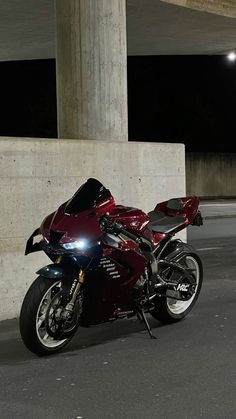 a red motorcycle parked in front of a concrete wall under an overpass at night