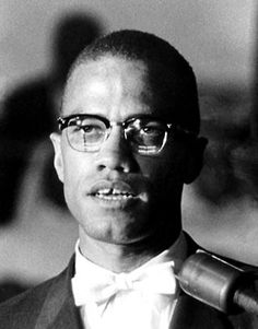 a man wearing glasses and a bow tie is speaking into a microphone in a black and white photo