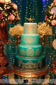 a blue and gold wedding cake sitting on top of a table next to vases filled with flowers