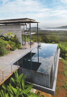 an outdoor swimming pool in front of a house with a wooden deck and glass walls