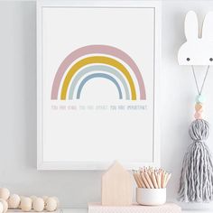 a white shelf topped with books and toys next to a framed rainbow art print on the wall