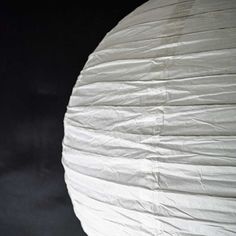 a large white paper lantern hanging from a black ceiling with one light on it's side