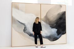 a woman standing in front of a large painting with black and white paint on it