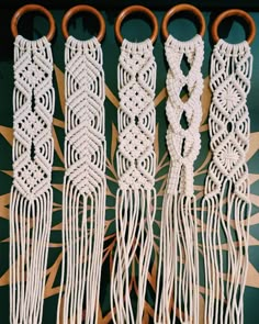 four white macrame tassels with wooden handles on a green and gold background