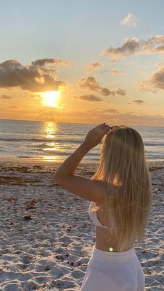 a woman standing on top of a sandy beach next to the ocean at sun set