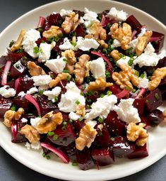 a white plate topped with beets, feta cheese and walnuts on top