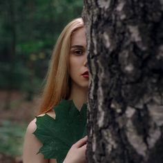 a woman is hiding behind a tree and looking at the camera while wearing a green leaf