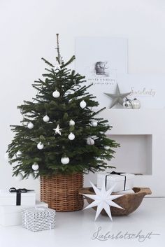 a small christmas tree in a wicker basket with white balls and ornaments around it