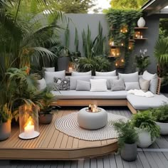 an outdoor living area with lots of plants and candles on the table in front of it