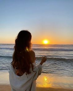 a woman standing on top of a sandy beach next to the ocean at sunset or sunrise