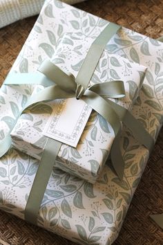 two wrapped presents sitting on top of each other with green ribbons and tags tied to them