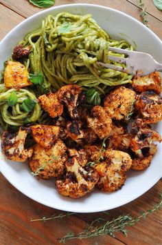 a white bowl filled with pasta and shrimp next to green pesto noodles on a wooden table