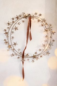 a metal wreath with stars hanging from it's side on a white wall surrounded by lights