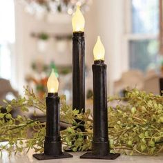 two black candles sitting on top of a table next to greenery and a chandelier