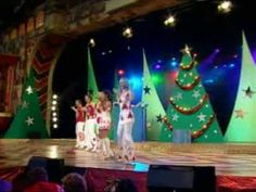 a group of people standing on top of a stage in front of christmas tree decorations