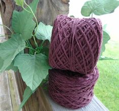 two balls of purple yarn sitting on top of a wooden bench next to a plant