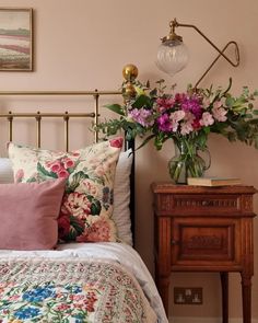 a bed with pink and green flowers on it next to a night stand, lamp and nightstand