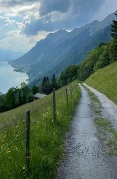 a dirt road going up a hill to a body of water with mountains in the background