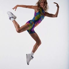 a woman jumping in the air while wearing a colorful swimsuit and white sneakers with her arms out