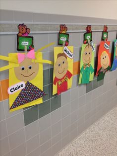 a row of children's artwork hanging on the wall in a school hallway with tile flooring