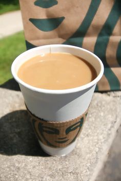 a cup of coffee sitting on top of a cement table next to a bag with a face drawn on it