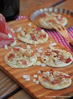 small pizzas are sitting on a wooden cutting board with cheese and meat toppings