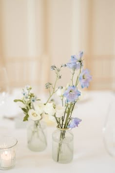 two vases filled with flowers on top of a table next to a glass candle