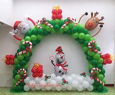 the balloon arch is decorated with green and white balloons, reindeers, and snowmen