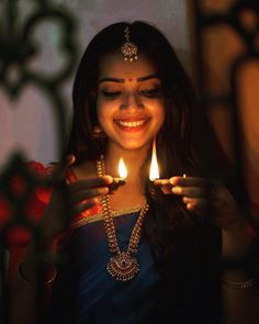 a woman holding a lit candle in her hands and smiling at the camera while wearing a blue sari