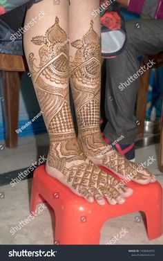 the legs and feet of a woman with henna tattoos on them, sitting on a stool