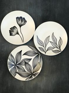 three black and white plates with flowers painted on them, sitting on a dark surface