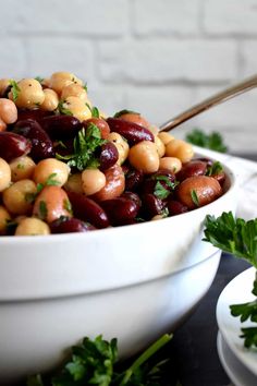 a white bowl filled with beans and parsley on top of a table next to plates