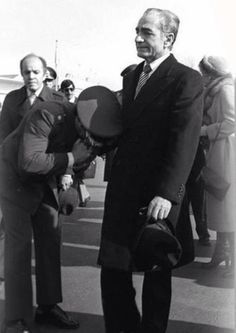 black and white photograph of two men in suits talking to each other on the tarmac