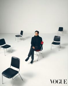 a man sitting on top of a black chair in front of several empty chairs and one red chair