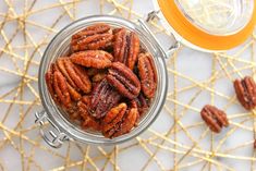 a glass jar filled with pecans sitting on top of a table next to an orange cup