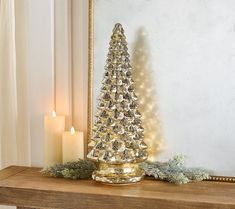 a gold christmas tree sitting on top of a mantle next to a mirror and lit candles