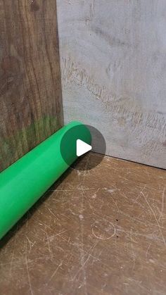 a green tube sitting on top of a wooden floor next to a piece of wood