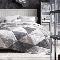 a bedroom with a large bed covered in grey and white quilts