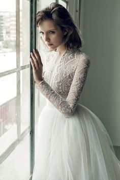 a woman in a white dress standing next to a window with her hands on her hips