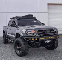 a grey toyota truck parked in front of a white garage door with its lights on