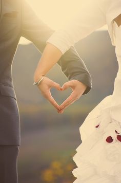 the bride and groom are holding their hands in the shape of a heart on their wedding day