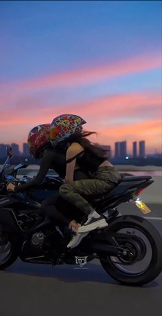 two people riding on the back of a motorcycle with an umbrella over their head at sunset