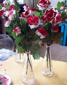 three clear vases with red and white flowers in them on a yellow table cloth