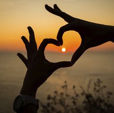 two hands making a heart shape with the sun setting in the background