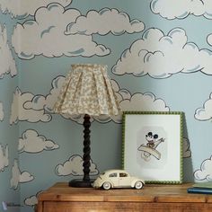 a lamp on top of a wooden dresser next to a wall with clouds and a car